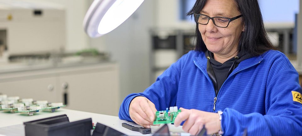 Mitarbeiterin bei der Qualitätskontrolle von bestückten Leiterplatten in der Elektronikfertigung von GLÜCK Industrie-Elektronik.